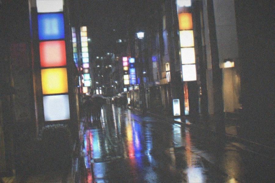 Crowded pavements in the Shinjuku nightlife district after dark, lit by the coloured glow of the buildings above