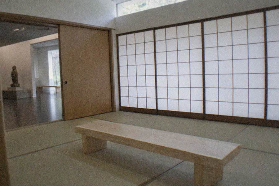 Visitors walking barefoot through a dark mirrored gallery with glowing floating spheres