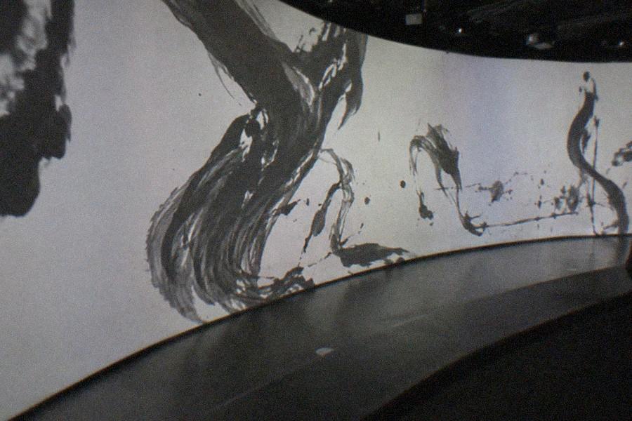 Visitors moving through a dark corridor where projected light and color flow across the floor at teamLab Borderless